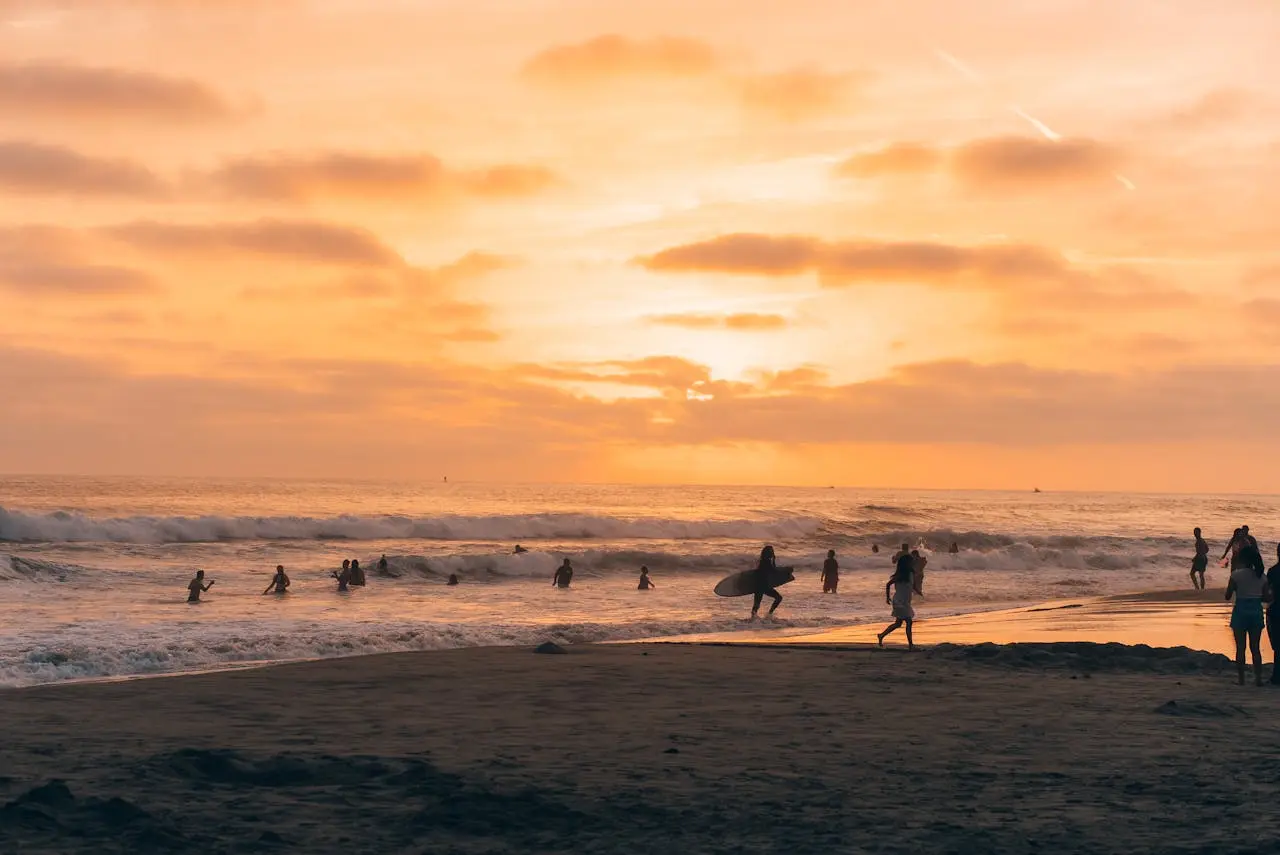 Carlsbad State Beach at golden hour with surfers and gentle waves.
